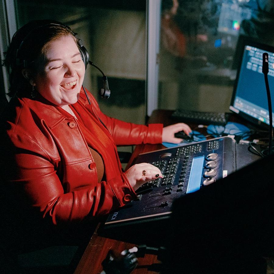 A student smiles while working in an audio production booth wearing a bright red jacket.